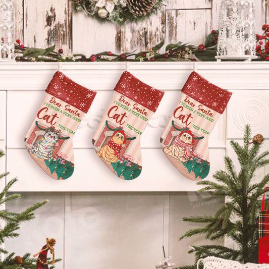 A cute personalized cat Christmas stocking that says 'Dear Santa, I've been a good cat this year', hung near a pretty Christmas tree and cozy fireplace.