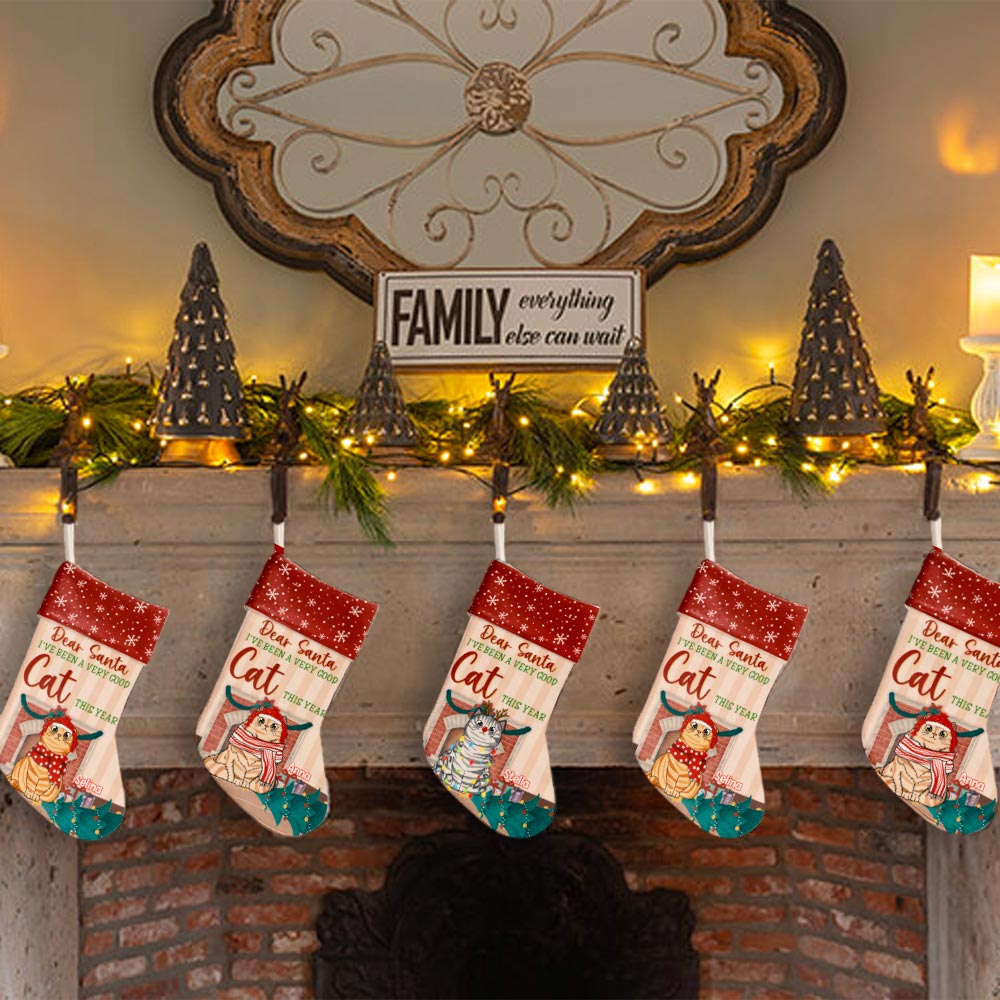 A cute personalized cat Christmas stocking that says 'Dear Santa, I've been a good cat this year', hung near a pretty Christmas tree and cozy fireplace.