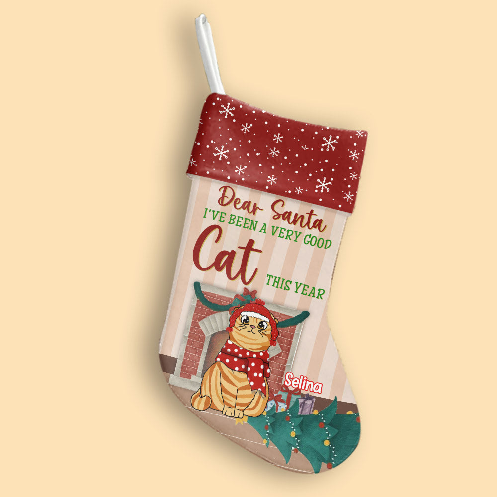 A cute personalized cat Christmas stocking that says 'Dear Santa, I've been a good cat this year', hung near a pretty Christmas tree and cozy fireplace.